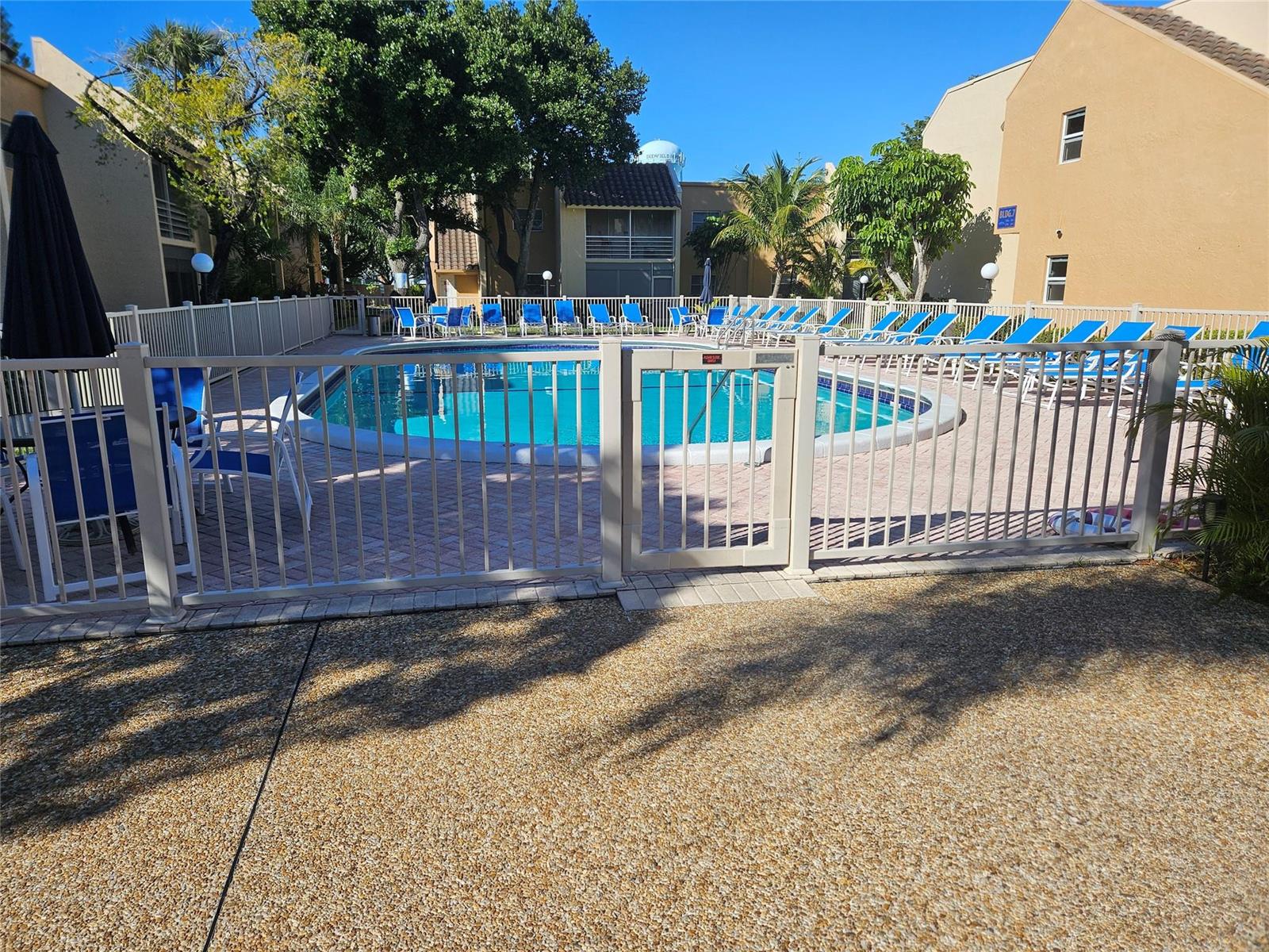 A fenced swimming pool area features blue lounge chairs on a brick patio — 959 SE 2nd Avenue # 117, Deerfield Beach FL 33441, DEERFIELD BEACH, FL