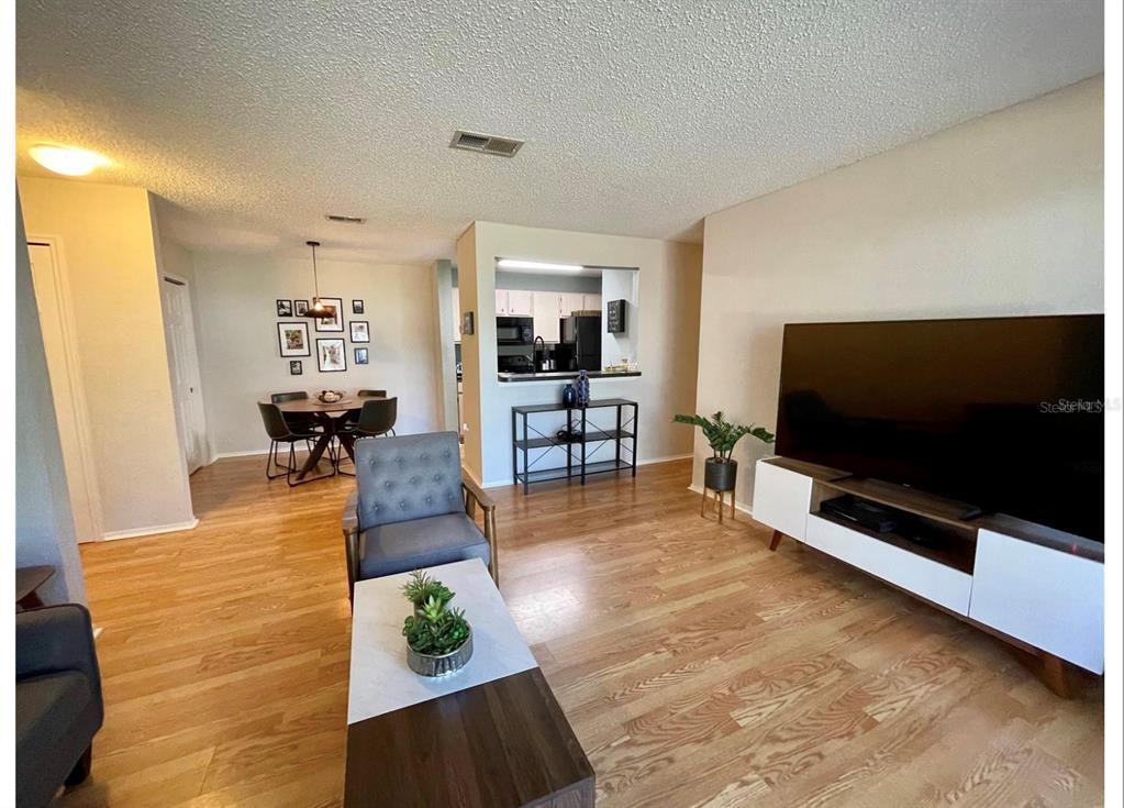 A living room with wood-look flooring, a large television, and an adjacent dining area — 3705 SW 27TH STREET UNIT 1113, GAINESVILLE, FL