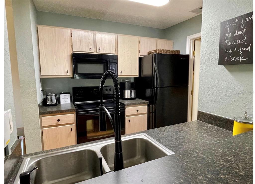 A kitchen features light wood cabinets, black appliances, dark countertops, and a double-basin sink — 3705 SW 27TH STREET UNIT 1113, GAINESVILLE, FL