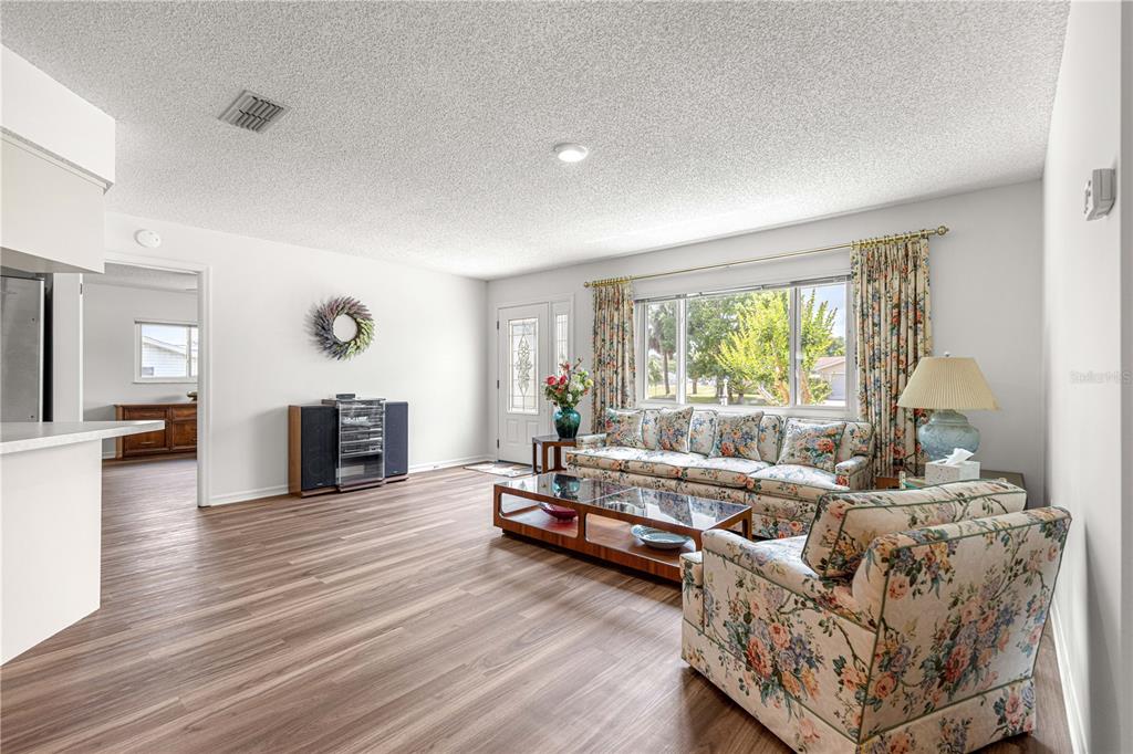 A living room with wood-look flooring, floral furniture, and a large window with curtains — 10956 SW 62ND TERRACE, OCALA, FL