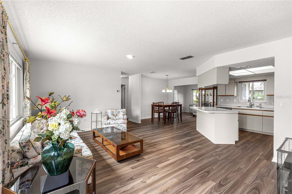 An open-concept living and dining area features wood-look flooring and a kitchen with white cabinetry — 10956 SW 62ND TERRACE, OCALA, FL