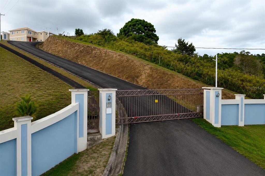 A paved driveway leads up a hill to a gated entrance with blue walls — ANTON RUIZ, HUMACAO, PR