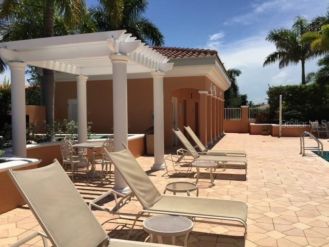A patio area features lounge chairs, a pergola, and a building with an orange exterior — 3191 MATECUMBE KEY ROAD UNIT 303, PUNTA GORDA, FL
