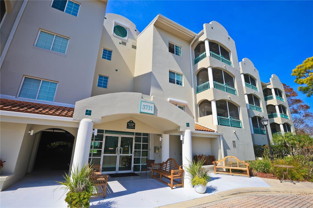 The exterior of a multi-story apartment building features a covered entrance with benches and balconies — 3731 SARASOTA SQUARE BOULEVARD UNIT 101E, SARASOTA, FL