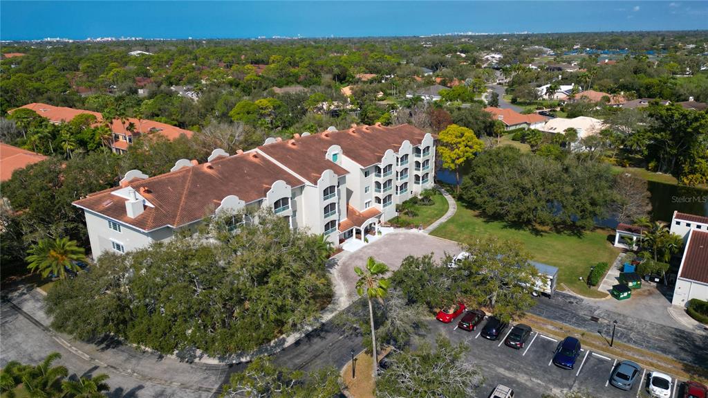 An aerial view shows a multi-story apartment building with a tiled roof and parking lot — 3731 SARASOTA SQUARE BOULEVARD UNIT 101E, SARASOTA, FL