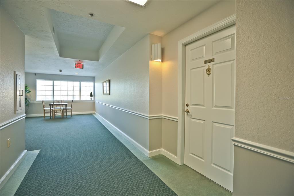 A hallway with green carpet, a white door labeled 101, and a small dining set — 3731 SARASOTA SQUARE BOULEVARD UNIT 101E, SARASOTA, FL