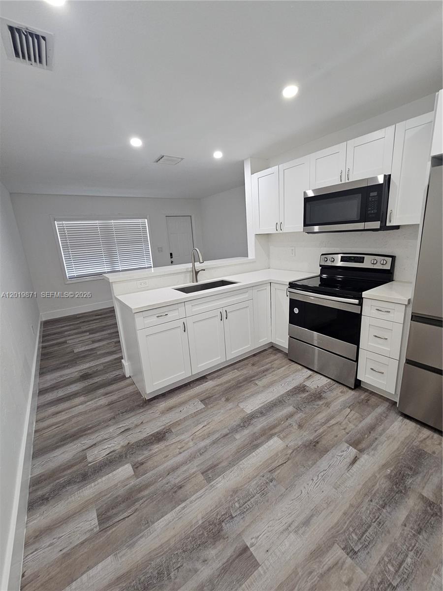A kitchen features white cabinets, stainless steel appliances, and wood-look flooring — 2030 Taylor St # 2030, Hollywood FL 33020, HOLLYWOOD, FL