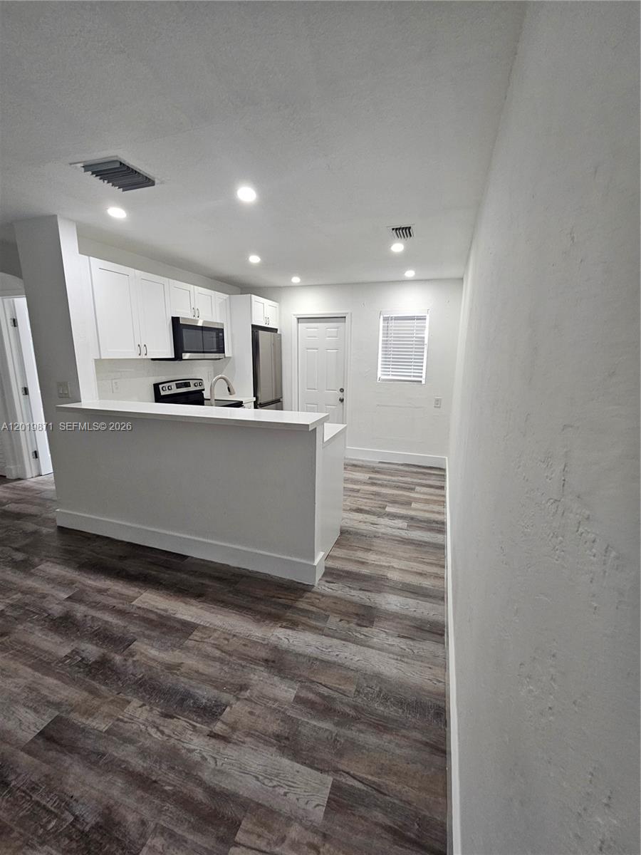 A kitchen features white cabinets, stainless steel appliances, a breakfast bar, and wood-look flooring — 2030 Taylor St # 2030, Hollywood FL 33020, HOLLYWOOD, FL