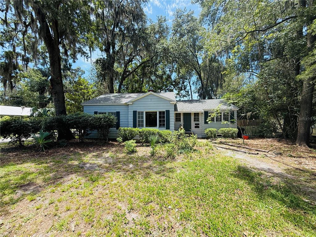 A light blue single-story house with dark shutters sits among large trees with Spanish moss — 745 NE 10TH AVENUE, GAINESVILLE, FL