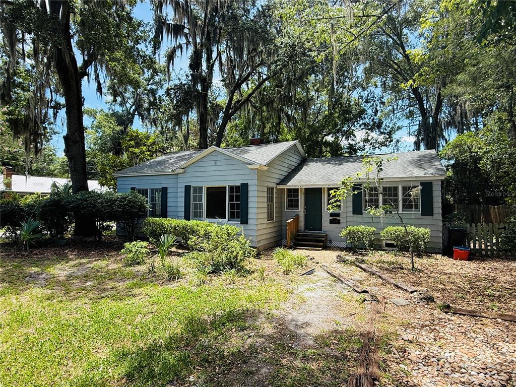 A light blue, single-story house with a gabled roof sits among trees and shrubs — 745 NE 10TH AVENUE, GAINESVILLE, FL