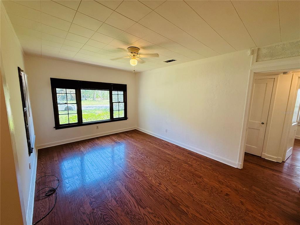 An empty room features hardwood floors, white walls, a ceiling fan, and black-framed windows — 745 NE 10TH AVENUE, GAINESVILLE, FL