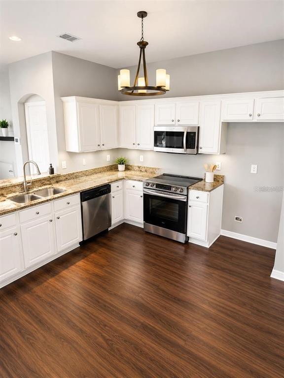 A kitchen features white cabinets, stainless steel appliances, granite countertops, and dark wood-look flooring — 11253 WINDSOR PLACE CIRCLE, TAMPA, FL