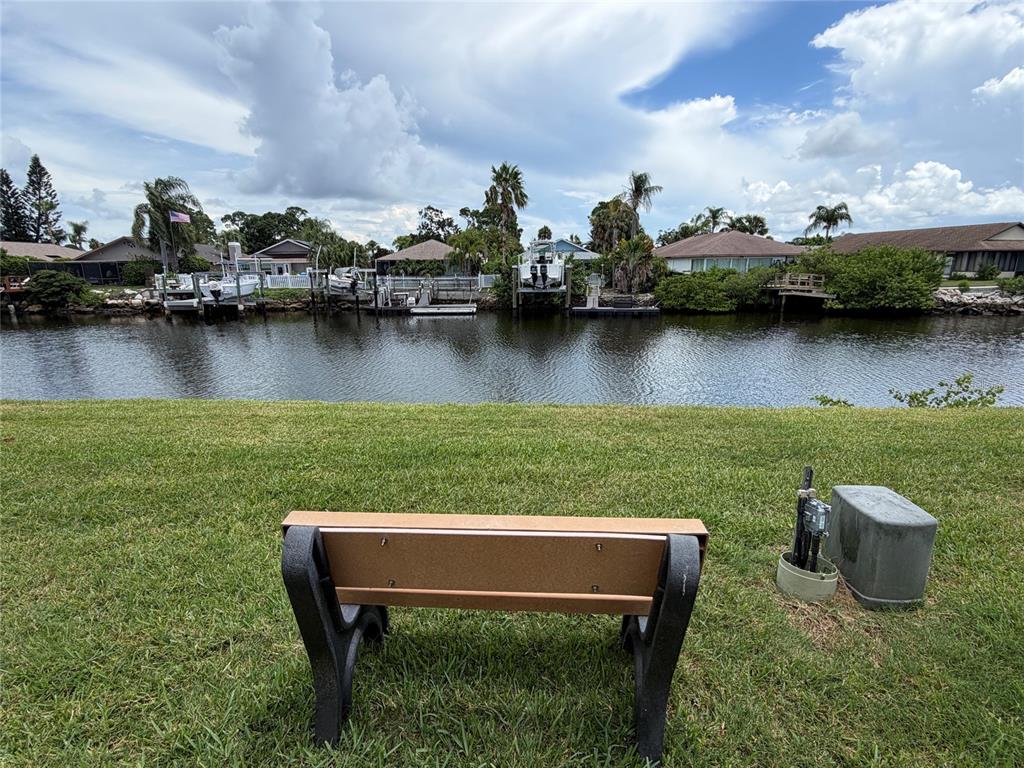 A park bench sits on a grassy lawn overlooking a canal with several docked boats — 4533 MARINE PARKWAY UNIT 204, NEW PORT RICHEY, FL