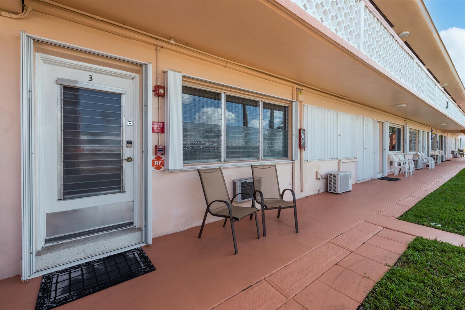 An exterior view of a motel-style building with a walkway, chairs, and numbered doors — 925 SW 11th Avenue # 3j, FL 33009, FL