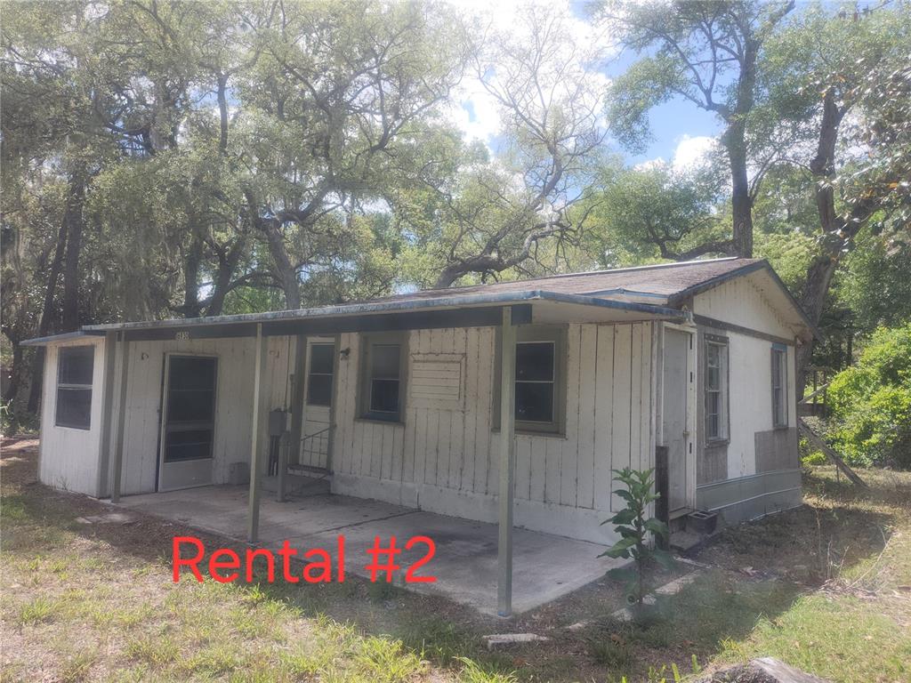 A weathered, single-story mobile home with a covered concrete porch sits among mature trees — 16930 SE 1ST LANE, SILVER SPRINGS, FL
