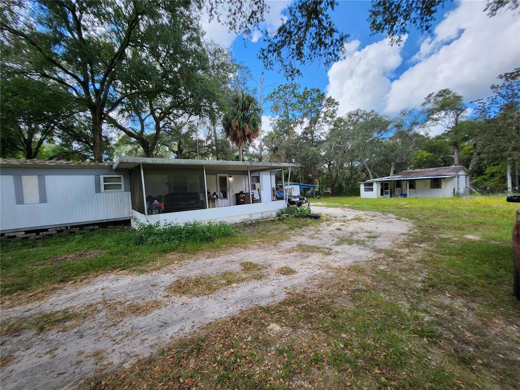 A mobile home with a screened-in porch sits on a dirt lot near another house — 16930 SE 1ST LANE, SILVER SPRINGS, FL