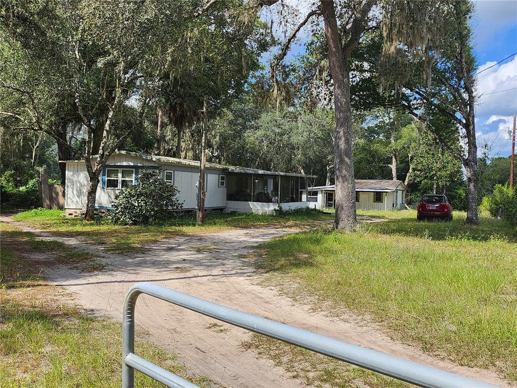 A mobile home with a screened porch sits on a dirt driveway among many trees — 16930 SE 1ST LANE, SILVER SPRINGS, FL
