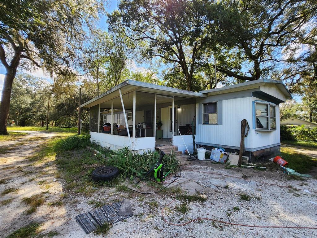 A single-story mobile home with a screened-in porch sits on a gravel lot under trees — 16930 SE 1ST LANE, SILVER SPRINGS, FL