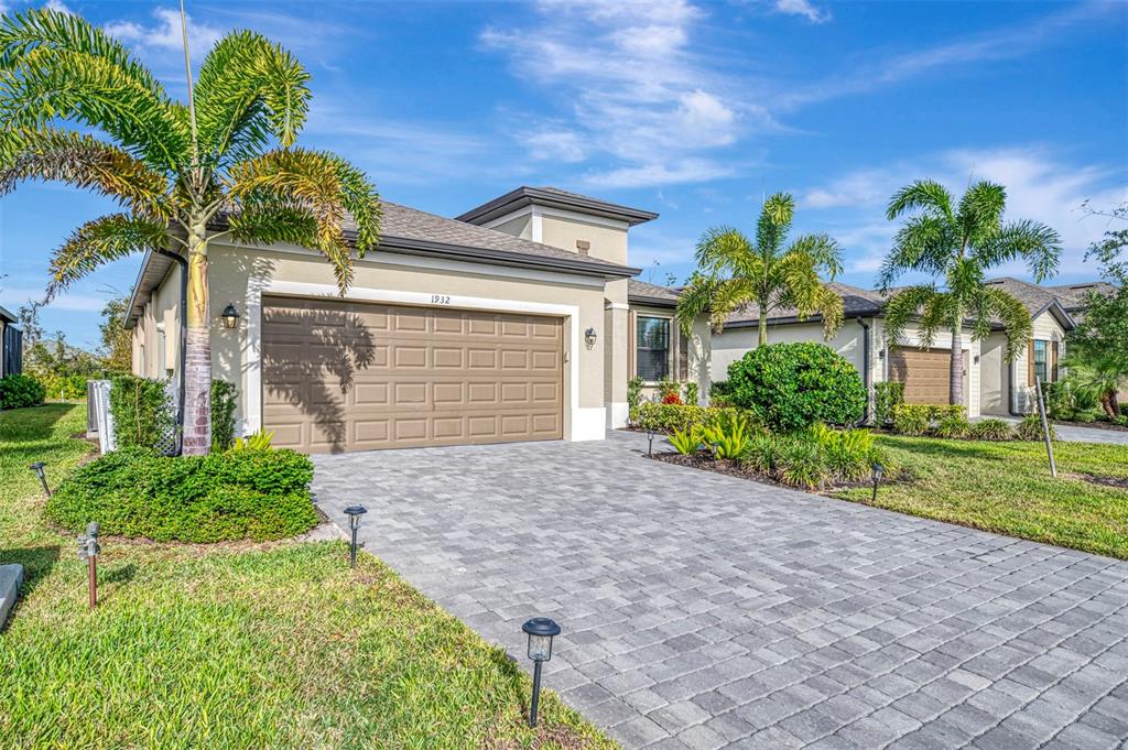 A tan single-story house with a paved driveway, a two-car garage, and palm trees — 1932 W ISLES ROAD, PORT CHARLOTTE, FL