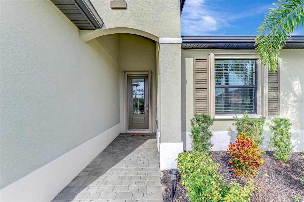 A paved walkway leads to the front entrance of a house with a glass-paneled door — 1932 W ISLES ROAD, PORT CHARLOTTE, FL