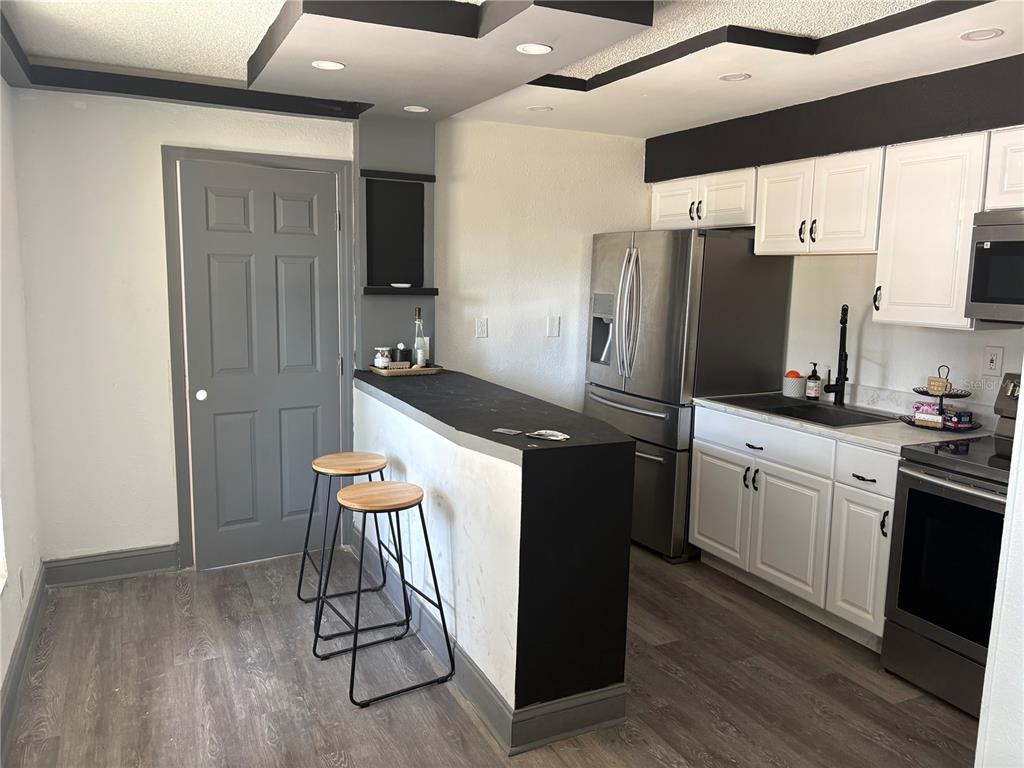 A kitchen features white cabinets, stainless steel appliances, a black breakfast bar, and gray flooring — 7019 N WILLOW AVENUE, TAMPA, FL