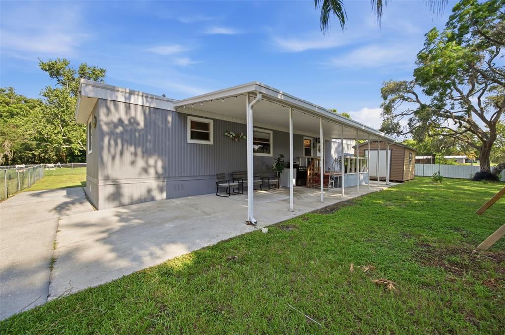 A gray mobile home features a long covered patio and a small storage shed outside — 9605 ANDY DRIVE, HUDSON, FL