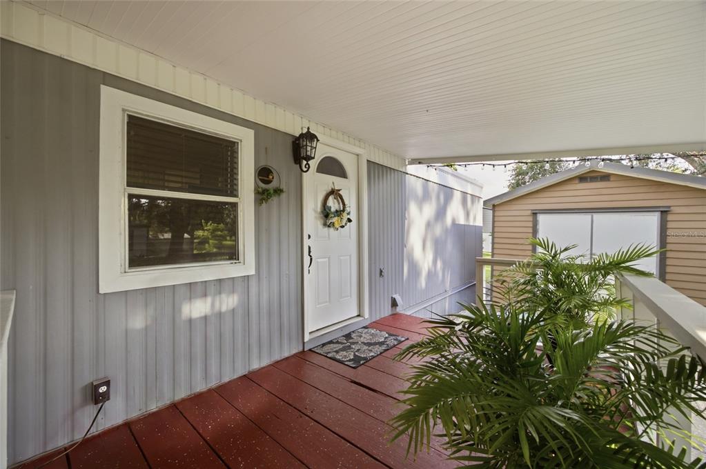 A covered wooden porch with a white front door, a window, and a potted palm plant — 9605 ANDY DRIVE, HUDSON, FL