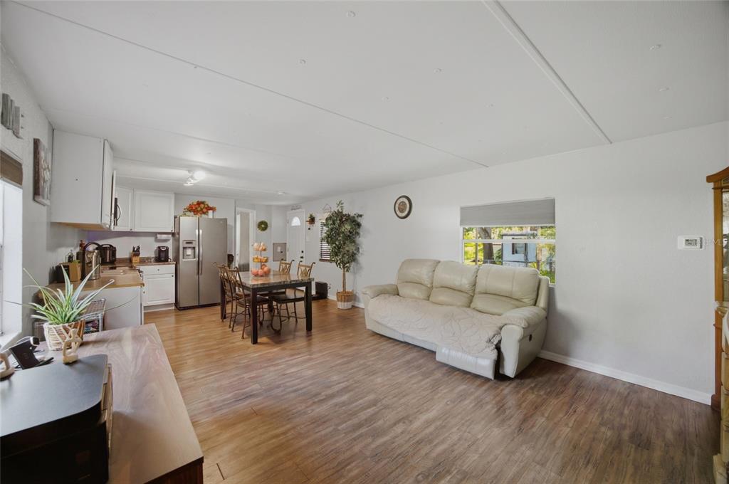 An open-concept living and dining area features light wood-look flooring, white walls, and a sofa — 9605 ANDY DRIVE, HUDSON, FL