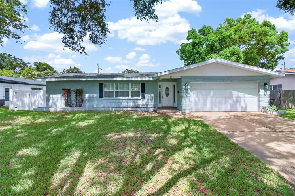 A single-story house with a light blue brick exterior, a white garage door, and a lawn — 700 RUSKIN ROAD, CLEARWATER, FL