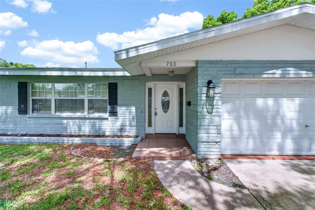 A single-story house exterior features light blue painted brick, a white front door, and garage — 700 RUSKIN ROAD, CLEARWATER, FL