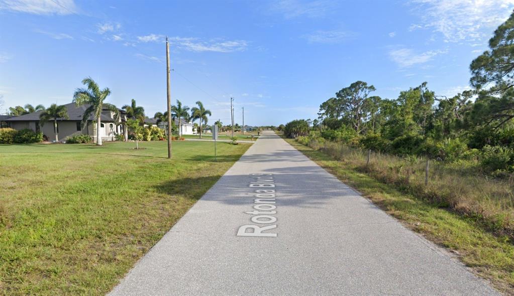 A paved road stretches into the distance past a residential house and wooded area — 285 ROTONDA BOULEVARD S, ROTONDA WEST, FL
