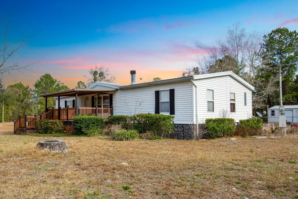 A white manufactured home with a wooden porch sits on a grassy lot at sunset — 2774 140TH TERRACE, LAKE CITY, FL
