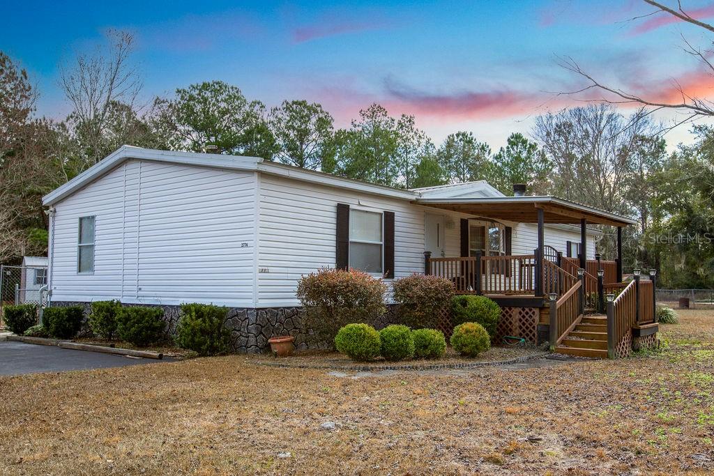 A single-story manufactured home with white siding, a stone-patterned base, and a wooden front porch — 2774 140TH TERRACE, LAKE CITY, FL