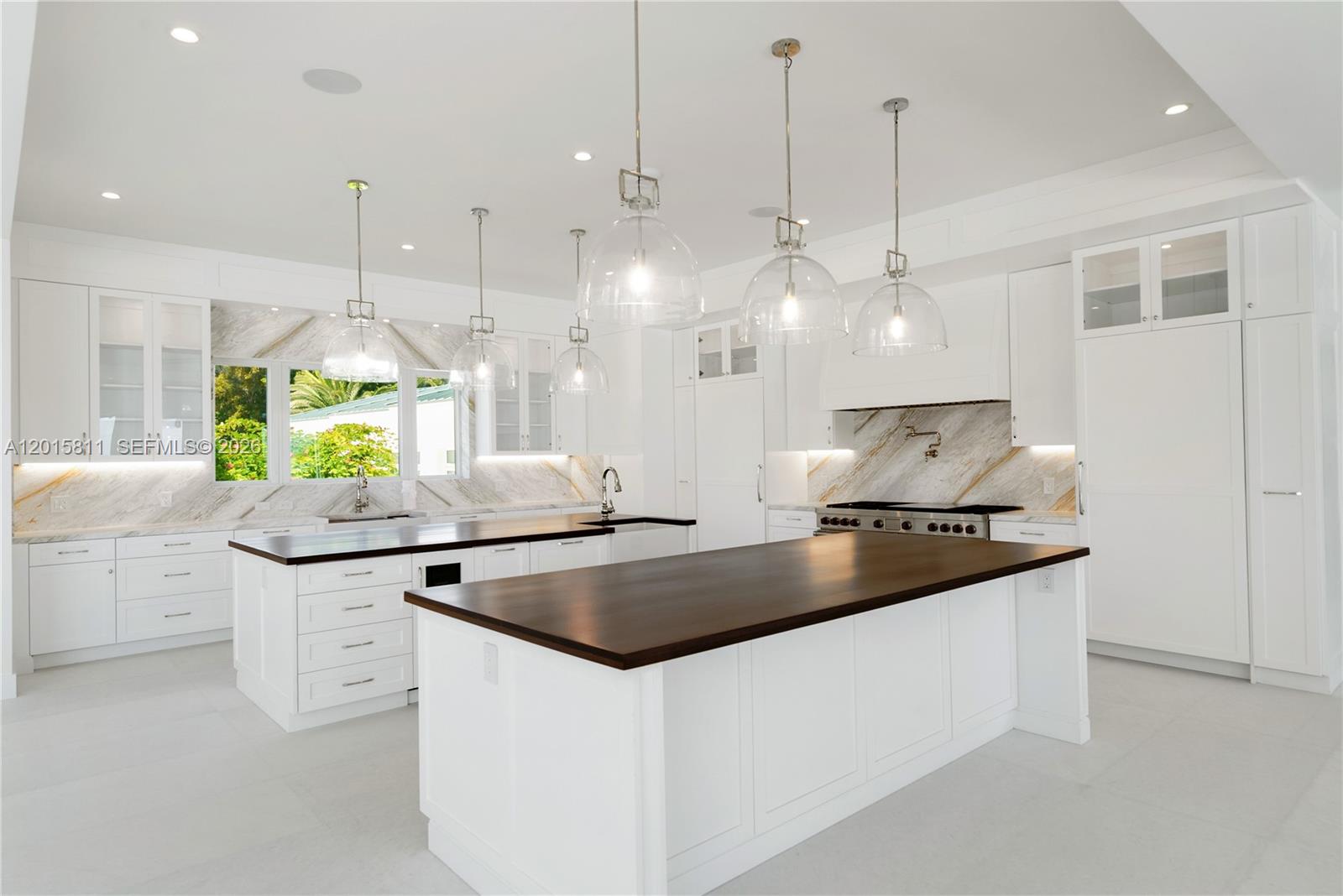 A bright kitchen features white cabinetry, marble backsplashes, and two islands with dark wood countertops — 88835/88845 Old Hwy, Tavernier FL 33070, TAVERNIER, FL