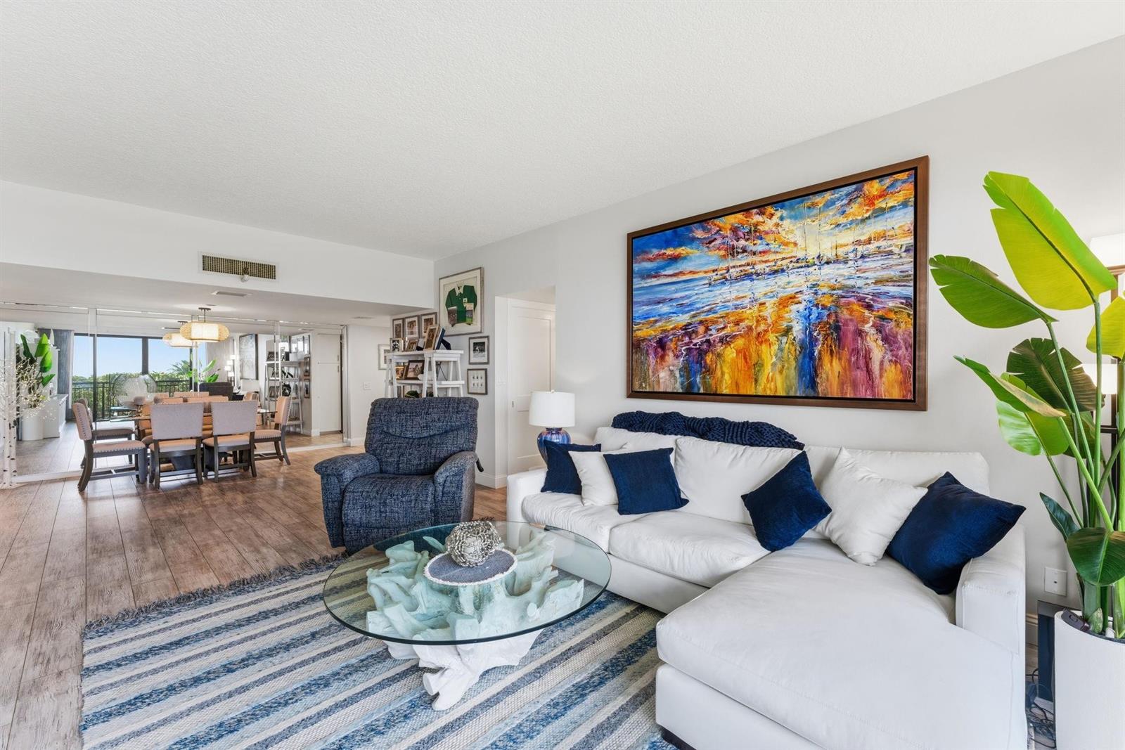 A living room features a white sectional sofa, blue recliner, glass coffee table, and large painting — 2727 N Ocean Boulevard Unit 301, Boca Raton FL 33431, BOCA RATON, FL