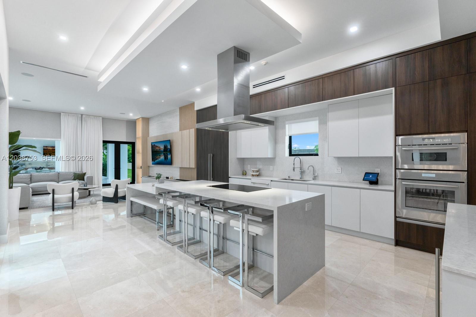 A modern kitchen features a large waterfall island, white cabinetry, and dark wood accents — 80 NW 129th Ave, Miami FL 33182, MIAMI, FL