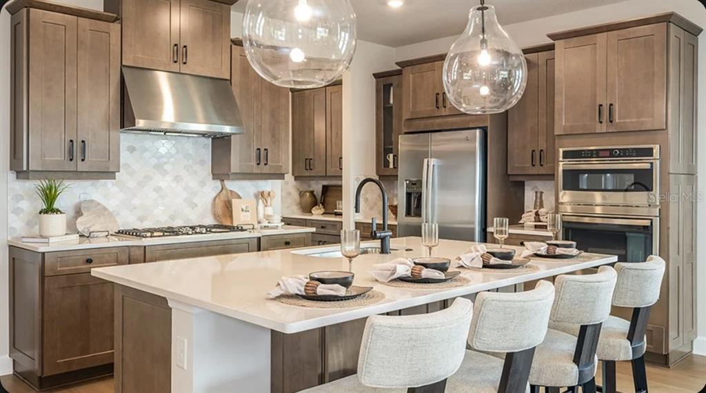 A modern kitchen features wood cabinets, a large white island, and stainless steel appliances — 11783 RALLY RANGE WAY, SAN ANTONIO, FL