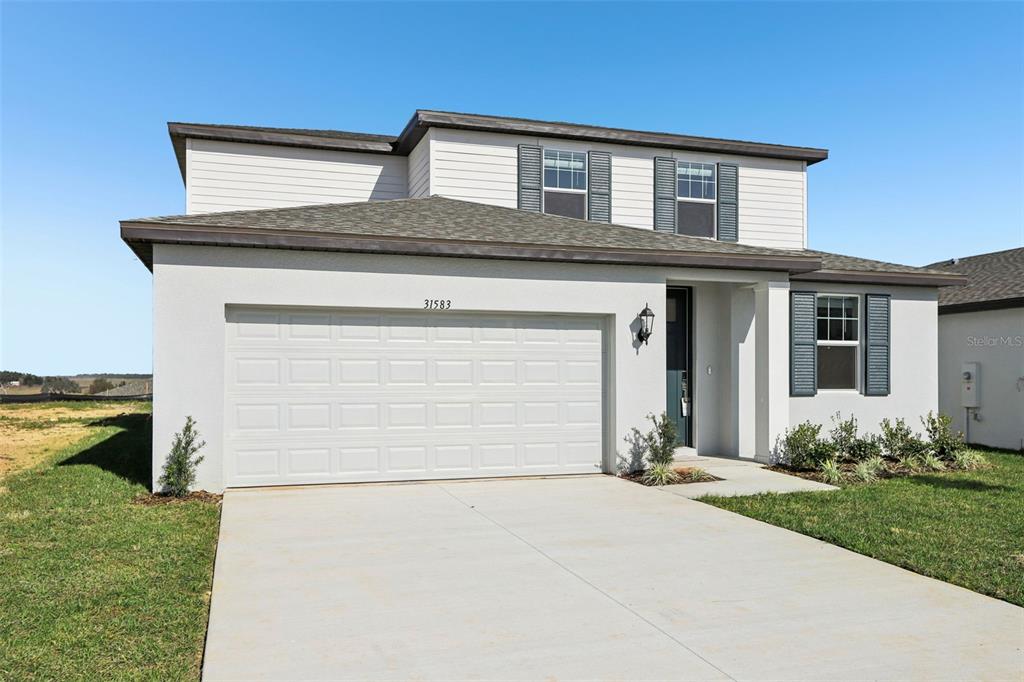 A two-story house with a white stucco exterior, a two-car garage, and dark shutters — 31583 WILD GRAPE LANE, BROOKSVILLE, FL