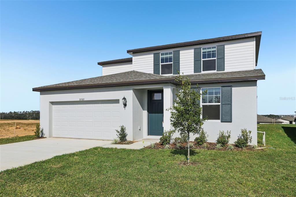 A two-story house with a gray stucco exterior, a two-car garage, and dark green shutters — 31583 WILD GRAPE LANE, BROOKSVILLE, FL