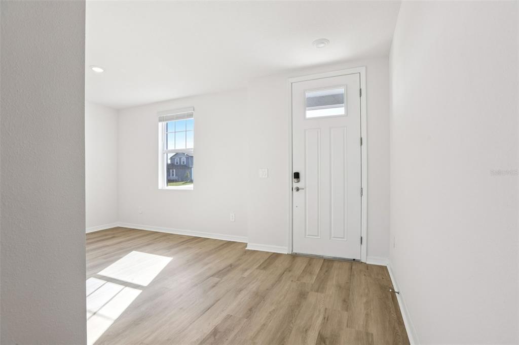 A bright, empty room features light wood-look flooring, white walls, and a white entry door — 31583 WILD GRAPE LANE, BROOKSVILLE, FL