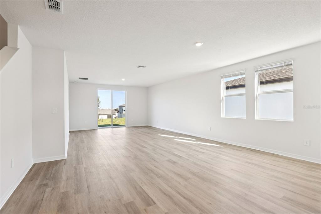 An empty living room features light wood-look flooring, white walls, and a sliding glass door — 31583 WILD GRAPE LANE, BROOKSVILLE, FL