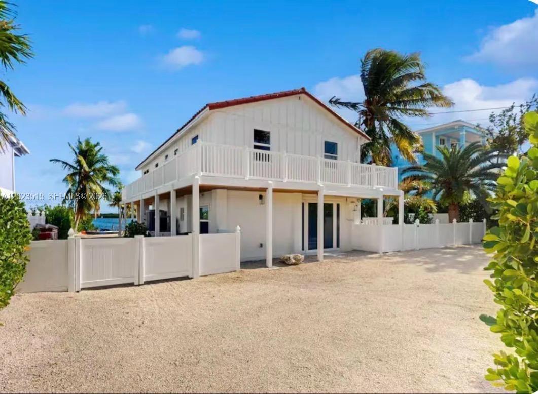 A two-story white house with a wrap-around balcony sits on a gravel lot — 128 La Paloma Rd, Key Largo FL 33037, KEY LARGO, FL