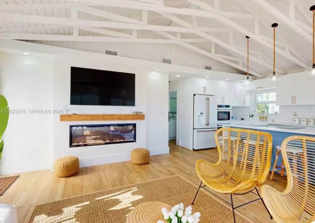 A living room with a fireplace, wall-mounted television, and wicker chairs under a vaulted ceiling — 128 La Paloma Rd, Key Largo FL 33037, KEY LARGO, FL