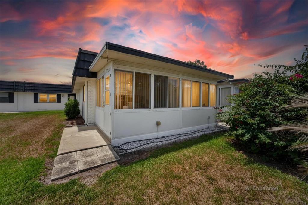 A white exterior sunroom with large windows sits on a grassy lot under a sunset — 301 KINGS BOULEVARD UNIT 138, SUN CITY CENTER, FL