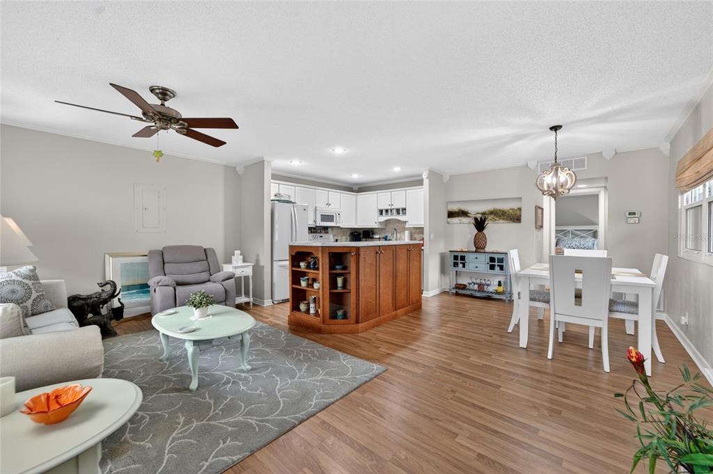 An open-concept living and dining area features wood-look flooring, a kitchen island, and white cabinetry — 301 KINGS BOULEVARD UNIT 138, SUN CITY CENTER, FL