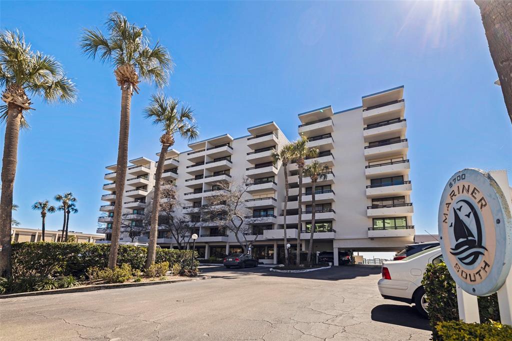 A multi-story apartment building with balconies stands behind a parking lot and palm trees — 5700 MARINER STREET UNIT 702 & 703, TAMPA, FL