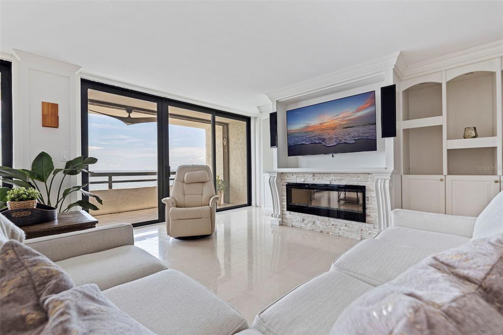 A bright living room features a fireplace, built-in shelving, and a balcony with ocean views — 5700 MARINER STREET UNIT 702 & 703, TAMPA, FL