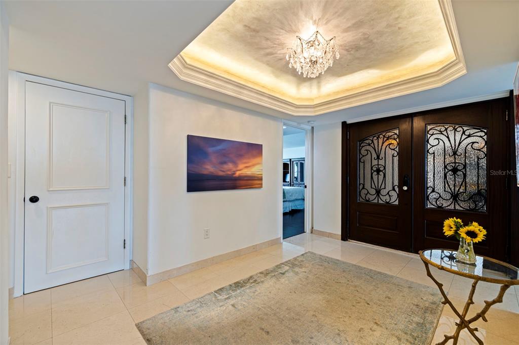 A bright foyer features a tray ceiling with a chandelier, tile flooring, and double doors — 5700 MARINER STREET UNIT 702 & 703, TAMPA, FL