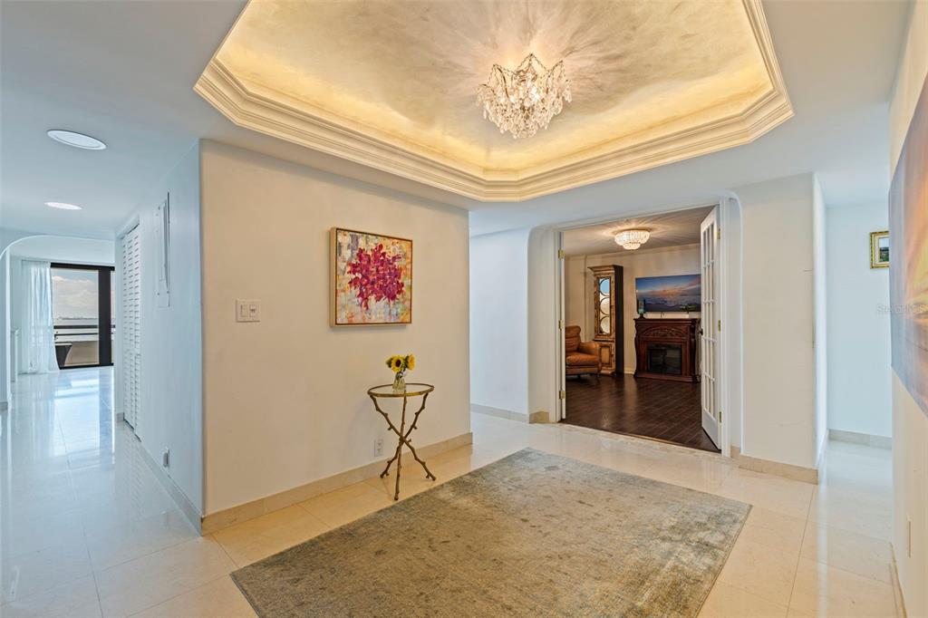 A bright foyer with a tray ceiling, crystal chandelier, and a rug on tile flooring — 5700 MARINER STREET UNIT 702 & 703, TAMPA, FL