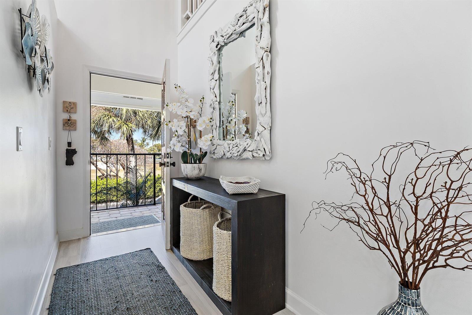 An entryway features a dark console table, a driftwood mirror, and a view of palm trees — 4161 S Us Highway 1 # E3, Jupiter FL 33477, JUPITER, FL